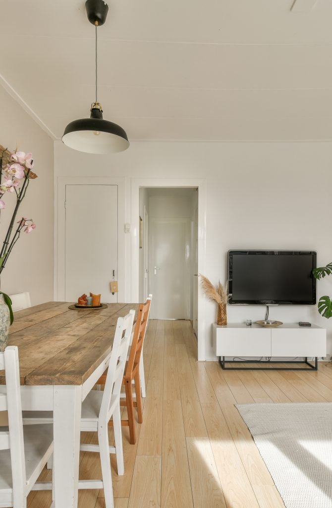 Shabby wooden table with chairs and vase located near comfortable couch against light walls with decorations and TV in modern apartment